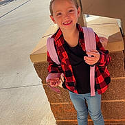 Michaela joined the competition — help win amazing prizes! child, smiling, backpack, red_jacket, blue_jeans, sneakers, outdoor, sunny, sidewalk, brick_wall, happy, young_girl, casual_clothing, daylight, urban, person, standing, street, school, portrait