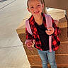 Michaela joined the competition — help win amazing prizes! child, girl, smiling, backpack, red_checkered_shirt, jeans, sneakers, outdoor, sidewalk, brick_wall, pillar, sunlight, happy, casual_clothing, portrait, young, daytime, person, standing, urban