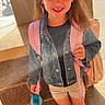 Michaela is registered to the contest to win money with this photo: child, girl, backpack, water_bottle, denim_jacket, shorts, sneakers, smiling, outdoor, sunlight, lens_flare, sidewalk, brick_wall, casual_clothing, daytime, happy, standing, person, school_ready, summer