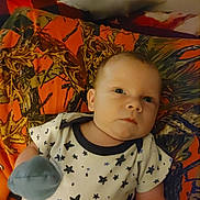 Finn is registered to the contest to win money with this photo: baby, infant, face, blue_eyes, onesie, star_pattern, blanket, orange, brown, mitten, lying_down, indoor, cute, child, person, young, newborn, apparel, soft_lighting, portrait