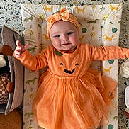 Mabel joined the competition — help win amazing prizes! baby, child, smile, orange_dress, headband, cute, indoor, changing_mat, animal_print, happy, infant, toddler, clothing, pattern, fabric, person, playful, reaching_hand, face, portrait