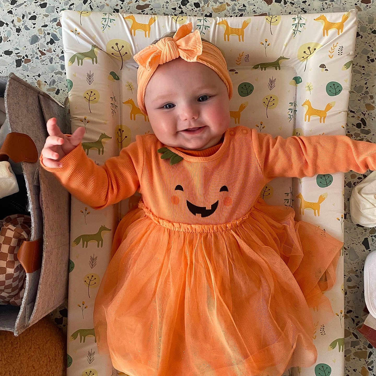 Mabel joined the competition — help win amazing prizes! animal_print, baby, changing_mat, child, clothing, cute, fabric, face, happy, headband, indoor, infant, orange_dress, pattern, person, playful, portrait, reaching_hand, smile, toddler