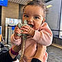 Skyler is registered to the contest to win money with this photo: baby, child, teething_toy, pink_sweater, curly_hair, indoor, hands, smile, happy, person, closeup, playful, cute, infant, holding, chewing, bright_eyes, toy, casual_clothing, warm_light