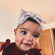 Skyler joined the competition — help win amazing prizes! baby, child, face, smile, headband, clothing, indoor, portrait, cute, closeup, person, happy, infant, young_child, eyelashes, button, skin, head, indoors, warm_lighting