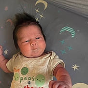 Ryley is registered to the contest to win money with this photo: baby, infant, child, cute, clothing, shirt, text, peas, fist, face, hair, lying_down, blanket, stars, moon, pattern, expression, indoors, newborn, person