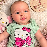 Athena joined the competition — help win amazing prizes! baby, infant, three_months, portrait, lying_down, hello_kitty, green_outfit, pink_bow, plush_toy, flowers, floral_background, milestone_photo, wooden_sign, smiling, wide_eyes, indoor, blanket, pastel_colors, close_up, child