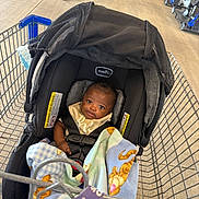 Camden is registered to the contest to win money with this photo: baby, car_seat, shopping_cart, blanket, infant, child, store, person, floor, walking, black_clothing, seatbelt, baby_bib, blanket_pattern, mesh_canopy, shopping, retail, indoor, cute, comfort