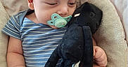 Leonidas joined the competition — help win amazing prizes! baby, infant, sleeping, pacifier, plush_toy, stuffed_animal, black_toy, striped_outfit, blue_clothing, blanket, pillow, cozy, bed, lying_down, portrait, indoors, soft_lighting, relaxed, baby_feet, watermark