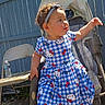 toddler, child, stroller, blue_dress, hello_kitty, headband, outdoor, sunlight, fence, folding_chair, water_bottle, curious, baby, person, sitting, casual, playful, daylight, portrait, clothing