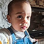 toddler, child, portrait, face, denim_overalls, sweater, indoor, stone_wall, fireplace, curly_hair, cute, expression, clothing, baby, person, head, closeup, light, young_child, casual