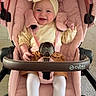 baby, stroller, pink, flower_headband, boots, smiling, child, indoor, cozy, cute, tights, yellow, brown_skirt, seatbelt, wheels, carriage, happy, infant, person, portrait