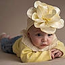 Fidjy a rejoint le concours — aidez-le/la à gagner de superbes lots ! baby, child, flower_headband, yellow_sweater, blue_eyes, portrait, infant, cute, soft_lighting, indoor, tummy_pose, headwear, clothing, skin, face, adorable, young_child, neutral_background, small_hands, looking