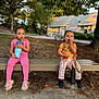 toddler, child, bench, outdoor, sitting, pink_clothing, orange_clothing, shoes, drink, cup, trees, building, sunlight, playful, face, person, nature, leaves, grass, side_by_side