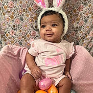 Mailani is registered to the contest to win money with this photo: baby, bunny_ears, pink_clothing, easter_eggs, colorful, floral_background, smiling, infant, cute, sitting, indoors, soft_lighting, playful, toy, headwear, child, holiday, festive, pastel_colors, happy