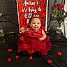 baby, background, black_cloth, celebration, child, cute, decor, event, face, flower_vase, headband, indoor, jewelry, photography, portrait, red_dress, rose_petals, roses, sitting, smiling