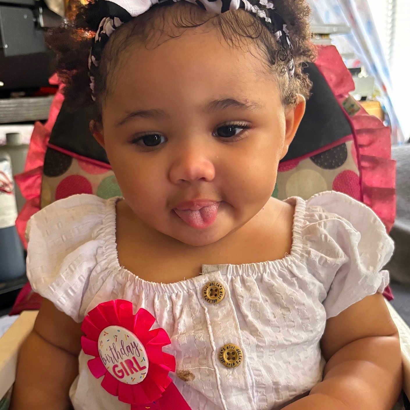 Aniree is registered to the contest to win money with this photo: baby, birthday, buttoned_shirt, celebration, child, curly_hair, cute, headband, high_chair, indoors, person, pink, playful, polka_dot, ribbon, seat, smiling, toddler, tongue_out, white_dress