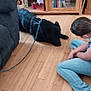 Penny joined the competition — help win amazing prizes! dog, black_dog, leash, person, indoor, wooden_floor, cabinet, dvd, sitting, jeans, furniture, flooring, casual, home, relaxing, pet, interaction, shelving, storage, leisure