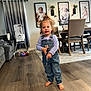 toddler, child, barefoot, denim_overalls, curly_hair, balloon, wooden_floor, living_room, dining_table, chairs, high_chair, curtains, plush_toy, framed_photos, portrait, indoor, person, home, floor, string