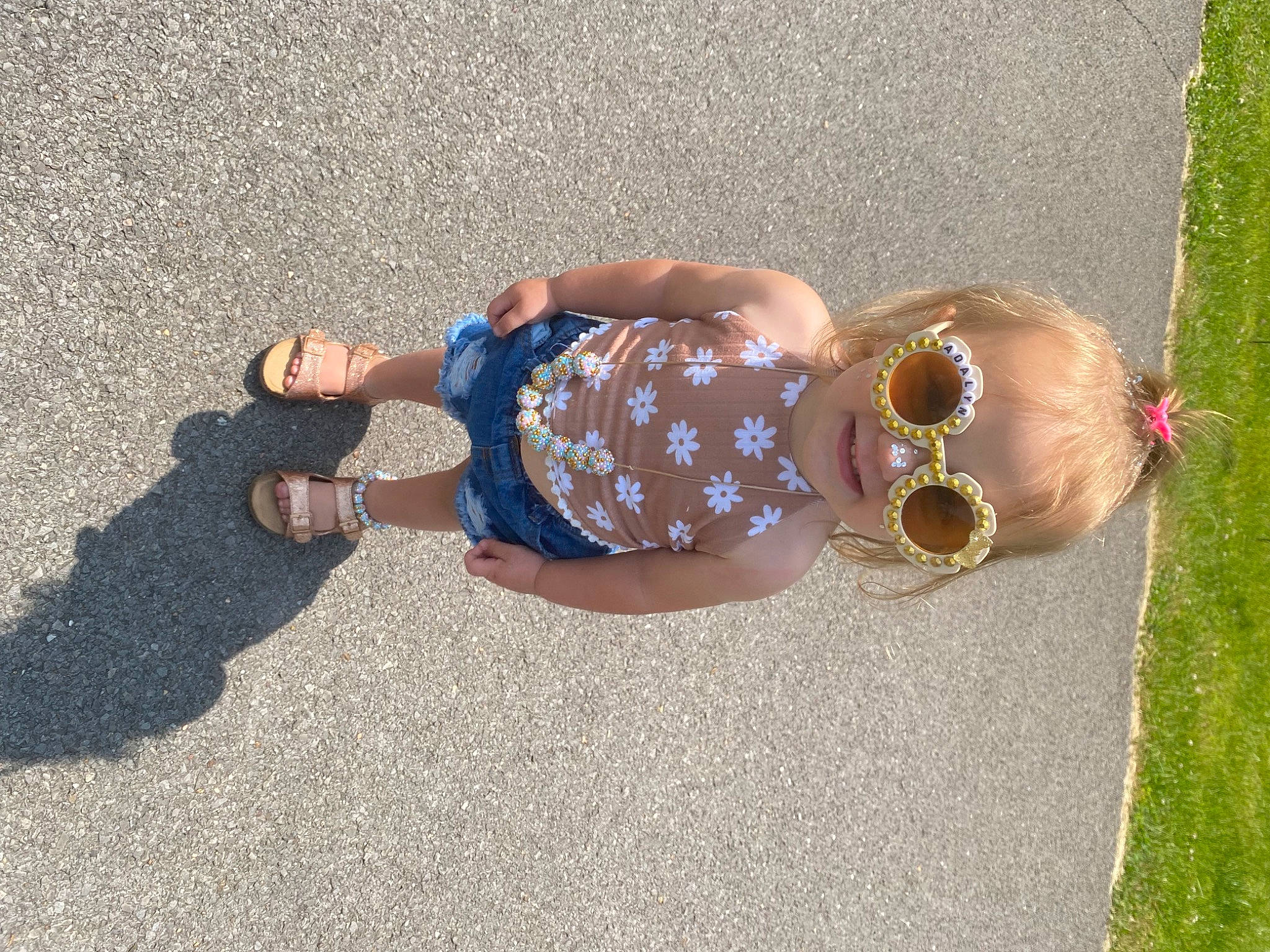 Adalyn Grace is registered to the contest to win money with this photo: asphalt, baby_toddler_clothing, child, eyewear, fashion_accessory, fawn, fun, goggles, grass, human_body, human_leg, jewellery, leisure, pattern, people_in_nature, person, road_surface, sidewalk, sunglasses, toddler