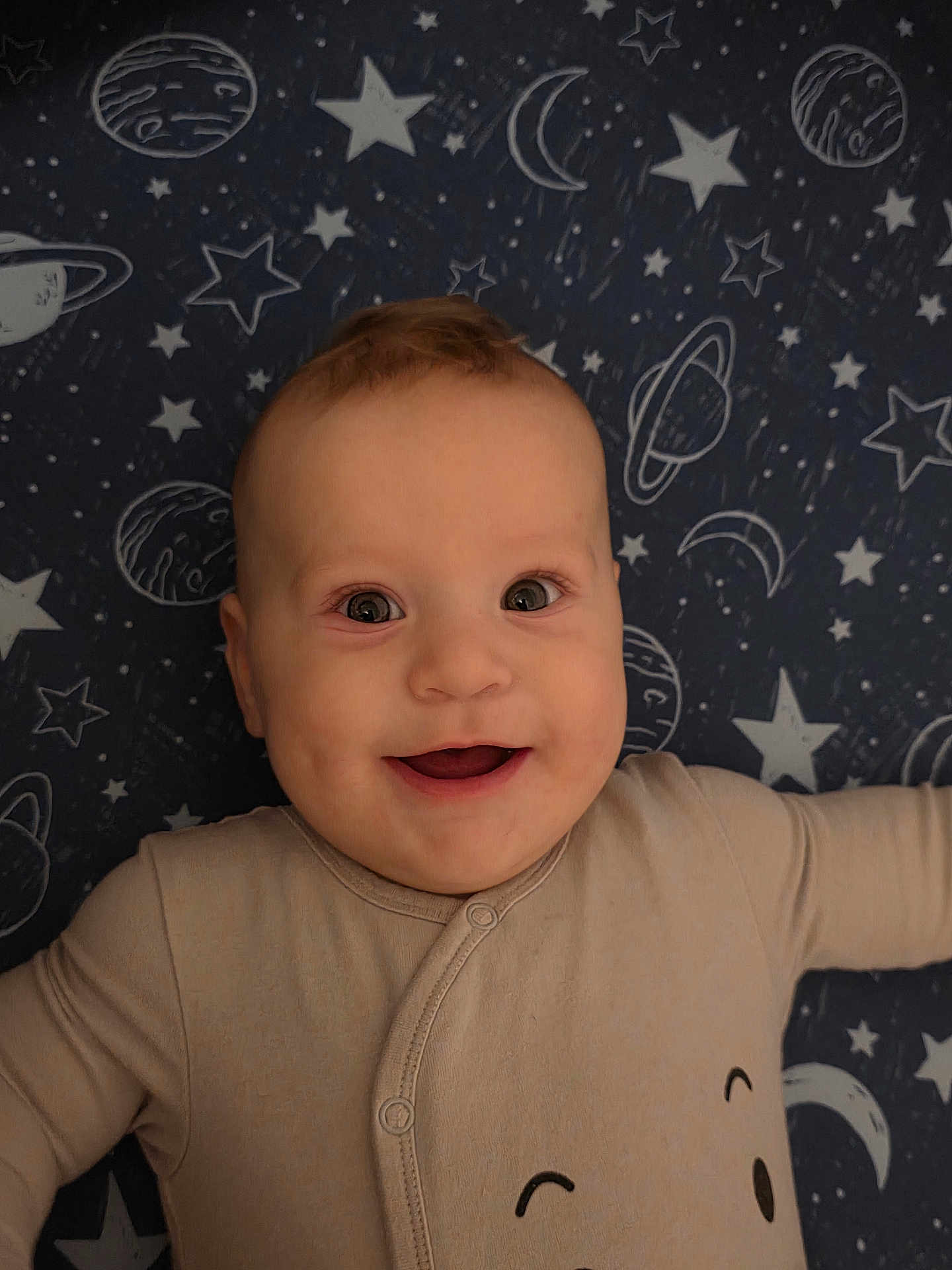 Damian is registered to the contest to win money with this photo: baby, smiling, infant, face, onesie, cosmic_background, stars, moons, planets, happy, child, portrait, cute, indoors, light_skin, short_hair, expression, clothing, lying_down, closeup