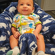 Jacob is registered to the contest to win money with this photo: baby, smiling, blanket, blue, white, dinosaur_onesie, socks, infant, indoor, cozy, happy, child, cute, portrait, furniture, living_room, soft, seated, warm_lighting, person