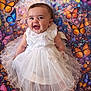 baby, background, butterflies, child, colorful, cute, dress, face, frilly, happy, infant, joyful, patterned_background, playful, portrait, sitting, smile, tulle, white_dress, young_child
