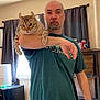 Kitkat is registered to the contest to win money with this photo: man, cat, indoor, curtains, furniture, tshirt, bald, beard, pet, holding, window, cabinet, sleeve, light, room, animal, domestic_animal, portrait, head, arm