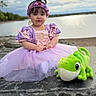 Daynelis is registered to the contest to win money with this photo: toddler, child, princess_dress, purple_dress, headband, flower_crown, plush_toy, green_frog, outdoor, lake, stone_ledge, cloudy_sky, portrait, cute, young_child, sitting, serene, nature, playful, costume