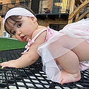 Daynelis is registered to the contest to win money with this photo: baby, balcony, brick_building, child, crawling, curious, cute, face, foot, grass, headband, infant, metal_table, outdoor, person, pink_clothing, railing, skin, table, tutu
