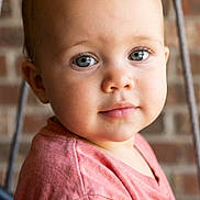 Jayda is registered to the contest to win money with this photo: toddler, child, portrait, face, blue_eyes, pink_shirt, short_hair, indoor, brick_wall, cute, baby, person, young_child, expression, casual_clothing, close_up, looking_at_camera, soft_lighting, warm_tones, head_and_shoulders