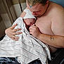 Jerry is registered to the contest to win money with this photo: newborn, baby, father, hospital_blanket, skin, tattoo, hat, holding, bonding, chair, person, indoor, comfort, love, family, newborn_hat, striped_blanket, caring, parent, portrait
