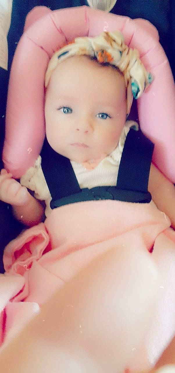 Estelle is registered to the contest to win money with this photo: arm, baby, blond, brown_hair, cheek, child, doll, eye, face, finger, flower, forehead, hand, head, iris, person, pink, plant, skin, toddler