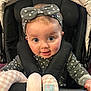 baby, child, polka_dot, headband, stroller, soft_toy, checkered, clothing, cute, face, infant, person, seatbelt, happy, portrait, indoor, pink, gray, pattern, smile