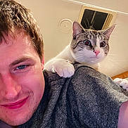 Theo is registered to the contest to win money with this photo: man, cat, indoor, shoulder, pet, smile, closeup, person, animal, feline, casual, friendly, grip, young_adult, expression, hair, clothing, portrait, whiskers, light