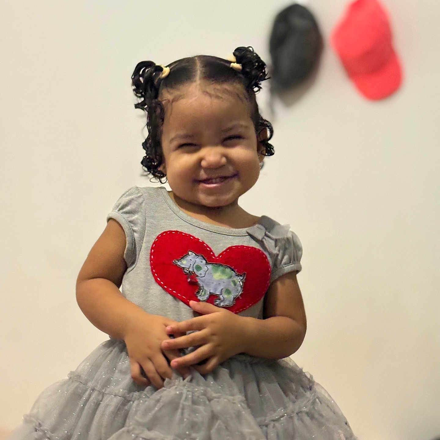 Alanna participe au concours pour gagner de l'argent avec cette photo : background, caps, child, clothing, curly_hair, cute, dress, fashion, gray_dress, happy, heart_patch, indoor, person, pigtails, portrait, smiling, standing, toddler, wall, young_child