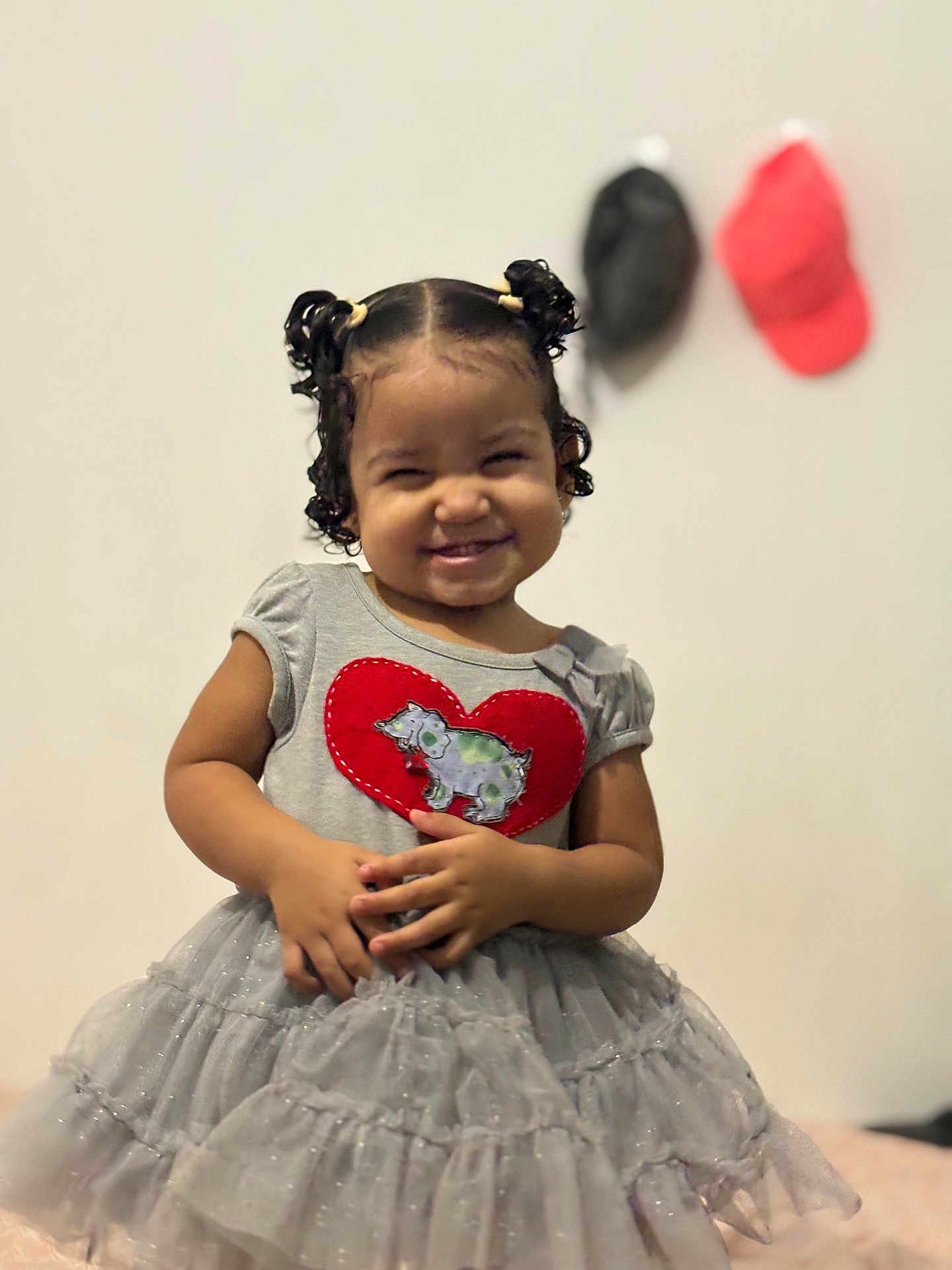 Alanna participe au concours pour gagner de l'argent avec cette photo : toddler, child, smiling, dress, pigtails, curly_hair, heart_patch, indoor, wall, caps, gray_dress, cute, happy, portrait, standing, person, clothing, background, fashion, young_child
