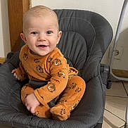 Aylan participe au concours pour gagner de l'argent avec cette photo : baby, child, smiling, orange_clothing, tiger_print, onesie, baby_rocker, gray, padded, floor, tile, indoor, happy, cute, infant, person, sitting, playful, face, eyes