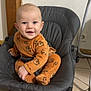 baby, child, smiling, orange_clothing, tiger_print, onesie, baby_rocker, gray, padded, floor, tile, indoor, happy, cute, infant, person, sitting, playful, face, eyes