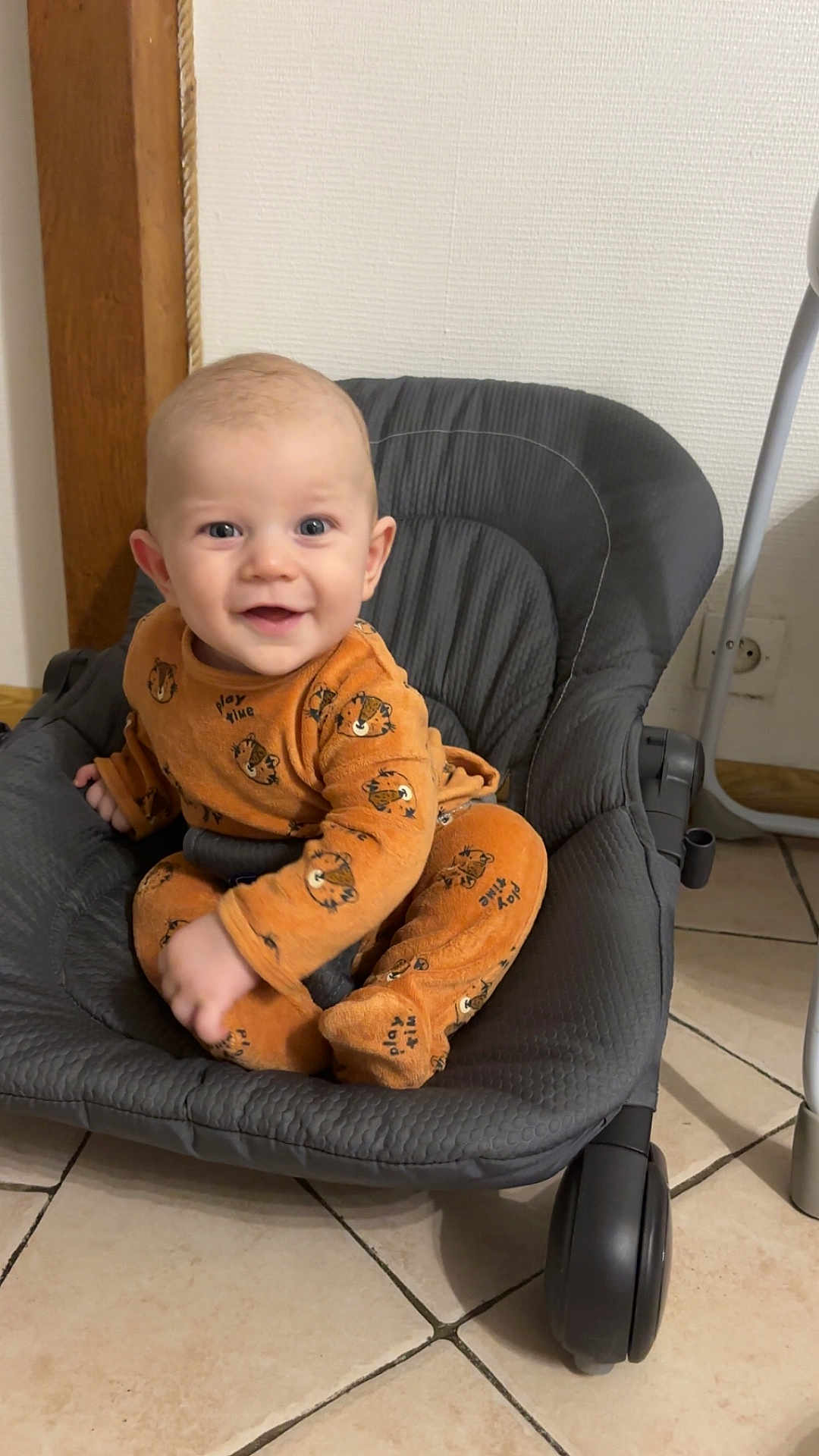Aylan participe au concours pour gagner de l'argent avec cette photo : baby, child, smiling, orange_clothing, tiger_print, onesie, baby_rocker, gray, padded, floor, tile, indoor, happy, cute, infant, person, sitting, playful, face, eyes