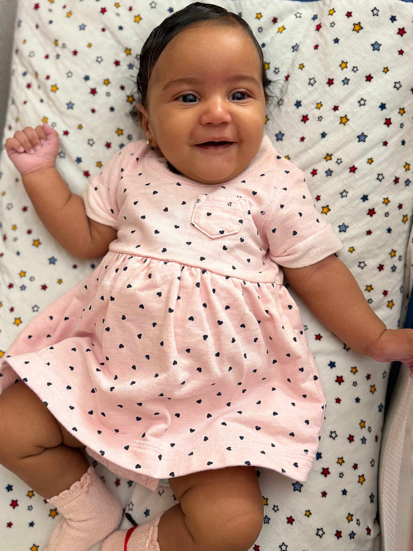 Amberly joined the competition — help win amazing prizes! baby, child, smiling, pink_dress, hearts_pattern, blanket, stars_pattern, lying_down, cute, happy, infant, earrings, short_hair, sock, soft_light, portrait, indoors, skin, face, hand