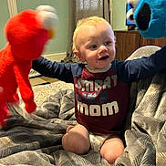 Blaize is registered to the contest to win money with this photo: toddler, child, puppet, elmo, cookie_monster, toy, blanket, indoor, smiling, happy, diaper, shirt, person, furniture, television, curtain, home, play, expression, candid
