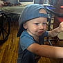 Blaize joined the competition — help win amazing prizes! toddler, child, boy, cap, blue_shirt, indoor, wooden_floor, table, chair, wheelchair, smiling, face, person, furniture, reaching, playful, room, casual_clothing, young_child, home