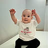 baby, child, tshirt, sitting, happy, smiling, arms_up, indoor, white_background, infant, cute, person, portrait, casual_clothing, bracelet, short_hair, real_doll_text, playful, young_child, minimalist