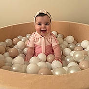 Lara a rejoint le concours — aidez-le/la à gagner de superbes lots ! baby, child, smiling, headband, pink_outfit, ball_pit, balls, beige, cream, white, indoor, happy, cute, infant, portrait, sitting, play, toy, childhood, joy