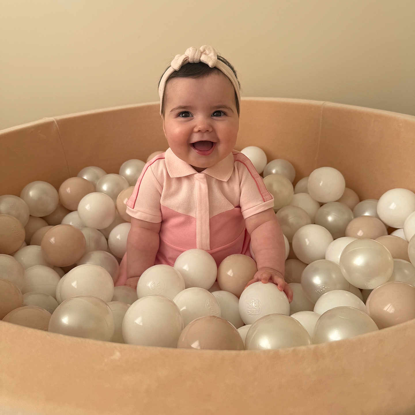 Lara a rejoint le concours — aidez-le/la à gagner de superbes lots ! baby, child, smiling, headband, pink_outfit, ball_pit, balls, beige, cream, white, indoor, happy, cute, infant, portrait, sitting, play, toy, childhood, joy