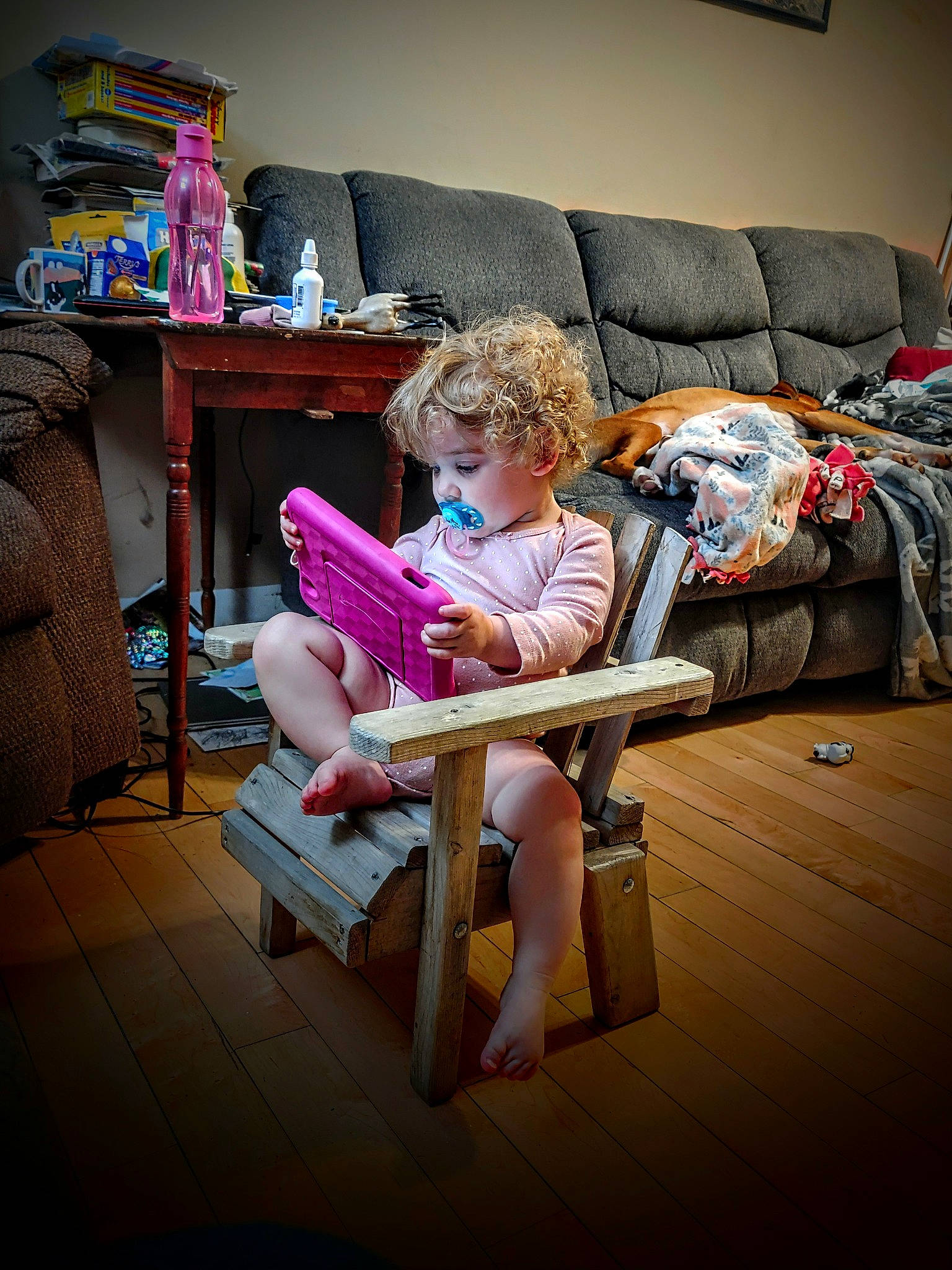 Karlie is registered to the contest to win money with this photo: child, comfort, couch, eyewear, flooring, fun, furniture, hardwood, human_leg, lap, leisure, living_room, outdoor_furniture, person, picture_frame, pillow, room, sandal, sitting, thigh