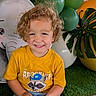 child, toddler, curly_hair, yellow_shirt, raccoon_graphic, balloons, cartoon_elephant, greenery, indoor, smiling, happy, portrait, grass, decor, party, cute, kid, casual_clothing, background, colorful
