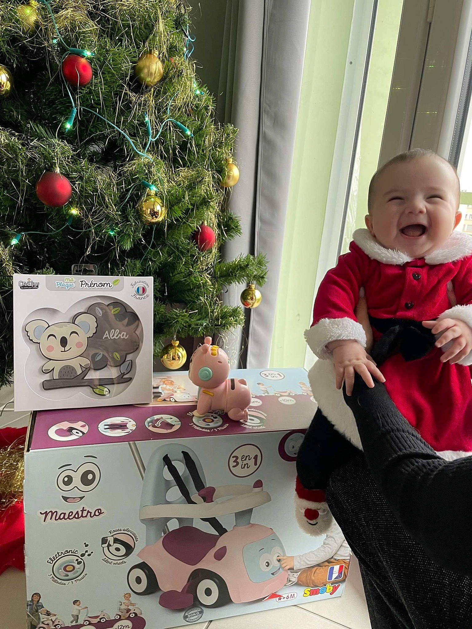 Alba participe au concours pour gagner de l'argent avec cette photo : baby, baby_toddler_clothing, christmas, christmas_decoration, christmas_eve, christmas_ornament, christmas_tree, event, happy, head, holiday, holiday_ornament, lap, ornament, person, plant, room, sleeve, smile, toddler