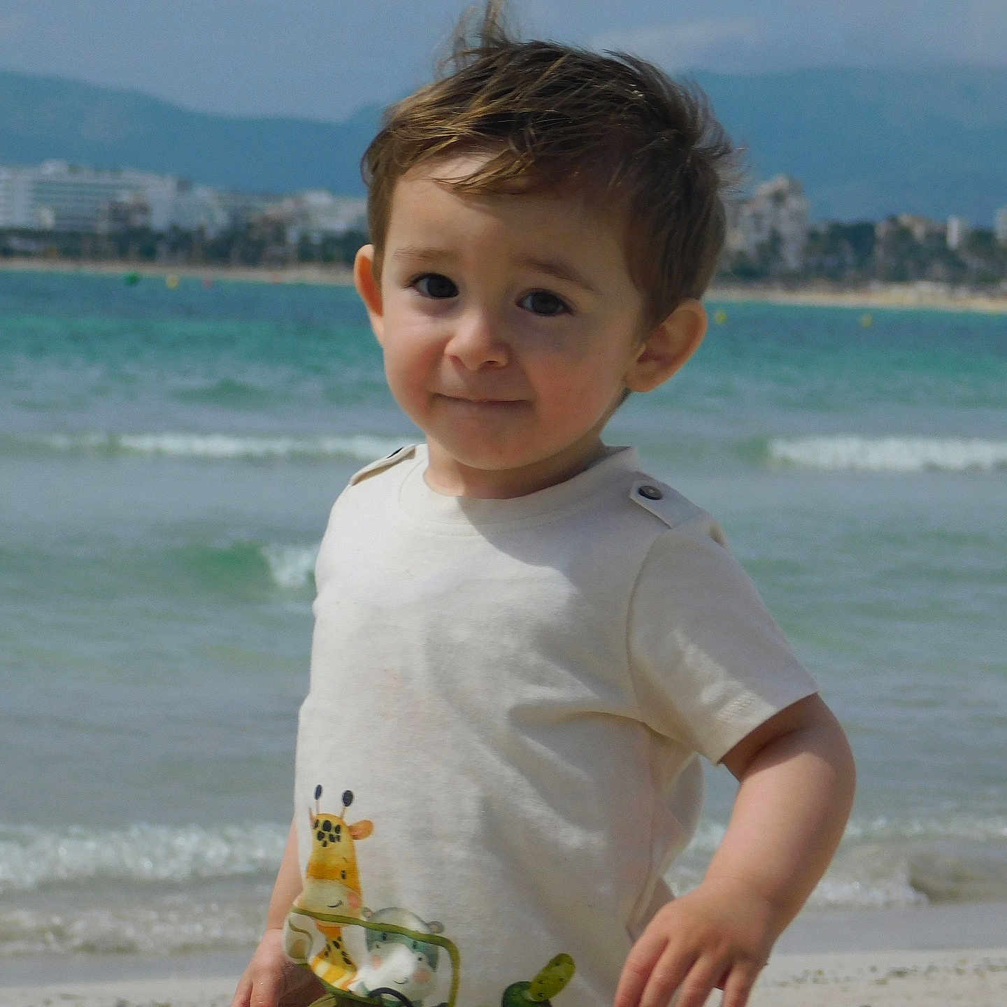 Nathan a rejoint le concours — aidez-le/la à gagner de superbes lots ! beach, buildings, casual_clothing, child, cityscape, daytime, nature, ocean, outdoor, portrait, sand, short_sleeve_shirt, sky, smile, summer, toddler, vacation, water, waves, young_child