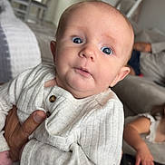 Alan is registered to the contest to win money with this photo: baby, child, infant, person, hand, clothing, pajamas, indoor, living_room, furniture, sofa, adult_hand, blurred_background, casual, cute, portrait, wide_eyes, expression, family, home